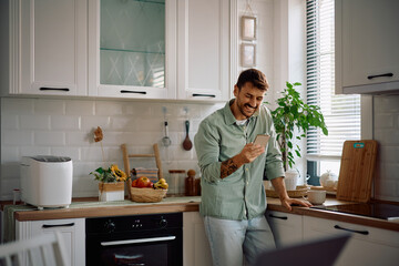 Happy man text messaging on cell phone in the kitchen.