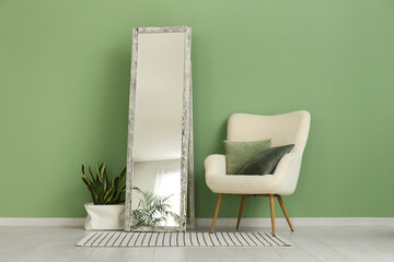 Floor mirror, armchair and houseplant near green wall in room
