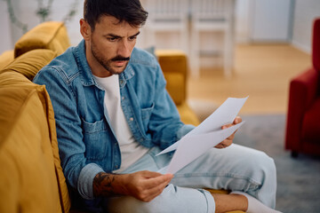 Displeased man going through his financial reports at home.