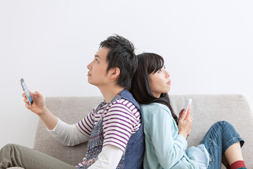 ソファで携帯電話を見る夫婦