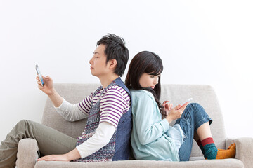 ソファで携帯電話を見る夫婦