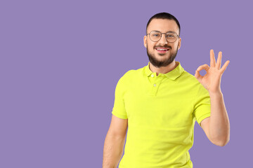 Handsome young man in eyeglasses showing OK gesture on lilac background