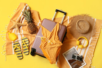 Composition with suitcase, swimsuit, pineapple and beach accessories on yellow background