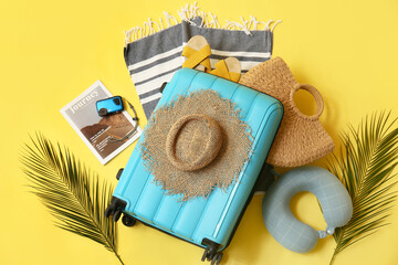 Composition with suitcase, tropical leaves and beach accessories on yellow background