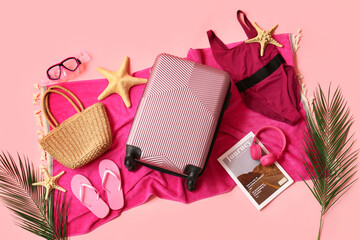 Composition with suitcase, swimsuit and beach accessories on pink background