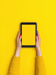 Person wearing yellow sweater holding a blank screen tablet against vibrant yellow background, creative tech concept with copy space.