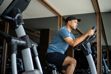Young fitness man workout with bicycle machine indoor gym. Male Exercise cardio on cycling machine....