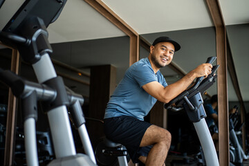 Young fitness man workout with bicycle machine indoor gym. Male Exercise cardio on cycling machine. Sport and health training in sport club
