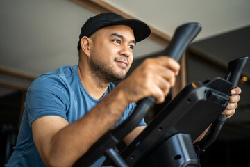 Young fitness man workout with bicycle machine indoor gym. Male Exercise cardio on cycling machine....