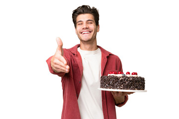 Young caucasian man holding birthday cake over isolated background shaking hands for closing a good...