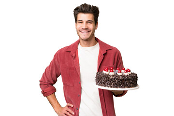 Young caucasian man holding birthday cake over isolated background posing with arms at hip and...