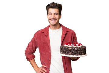 Young caucasian man holding birthday cake over isolated background posing with arms at hip and smiling