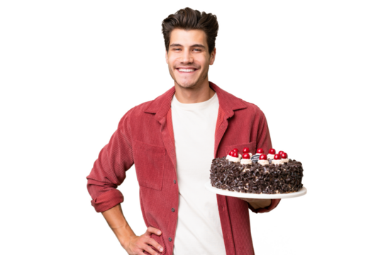 Young caucasian man holding birthday cake over isolated background posing with arms at hip and smiling
