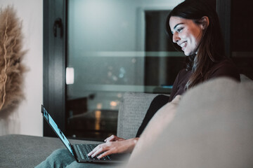 Young woman alone at home working late at night on her laptop. Freelancing, studying, chatting...