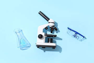 Modern microscope with safety glasses and flask on blue background