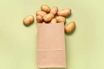 Paper bag with raw baby potatoes on green background