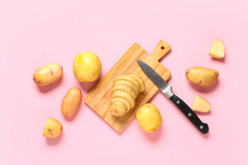 Wooden board with raw baby potatoes on pink background