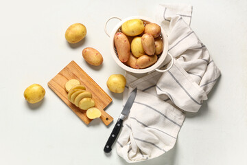 Wooden board and colander with raw baby potatoes on grey background