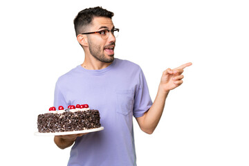 Young caucasian man holding birthday cake isolated on green chrome background intending to realizes...