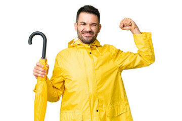 Young caucasian man with rainproof coat and umbrella over isolated background doing strong gesture