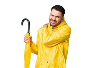 Young caucasian man with rainproof coat and umbrella over isolated background suffering from pain...