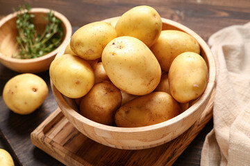 Bowl with raw baby potatoes and thyme on wooden background, closeup