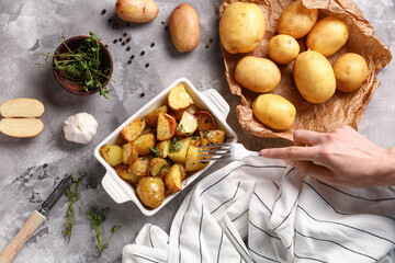 Female hand with fork and baking dish of baked baby potatoes on grey background