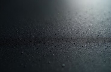 Close-up macro shot of dark textured surface with subtle water droplets. Fine grain, smooth yet rough feel. Sharp focus on intricate details, shadows, contrast create depth. Subtle grey tones enhance