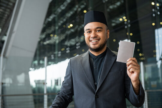 Muslim asian businessman traveler holding boarding pass ticket, passport and smartphone at the airport terminal with luggage. Cheerful tourist islamic at airport holiday trip.