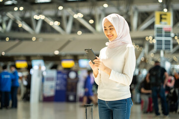 Muslim asian businesswoman traveler holding boarding pass ticket, passport and smartphone at the airport terminal with her luggage. Islamic cheerful tourist female having holiday trip weekend.