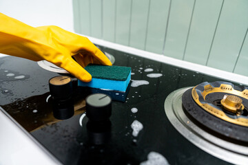 Hand woman cleaning the gas stove with sponge. Housekeeper cleaning kitchen