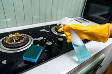 Hand woman cleaning the gas stove with sponge. Housekeeper cleaning kitchen