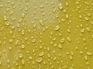 Close-up of water droplets on a smooth yellow surface after rain with scattered patterns
