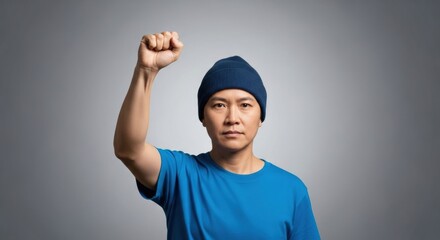 Asian young adult male demonstrating with raised fist in blue beanie and shirt