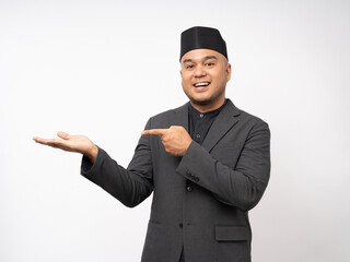 Portrait happy young asian muslim man pointing on isolated white background. Islamic Attractive Muslim man wearing songkok cap islam costume.