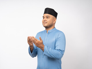Portrait happy young asian muslim man standing greeting pose on isolated white background. Islamic Attractive Muslim man wearing songkok cap islam costume and praying