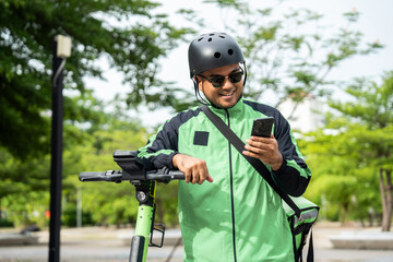 Rider food delivery man wearing green uniform and helmet ride the EV scooter delivery food service to customer. Happy delivery man with green backpack shipping of goods to customers by scooter