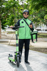 Rider food delivery man wearing green uniform and helmet ride the EV scooter delivery food service to customer. Happy delivery man with green backpack shipping of goods to customers by scooter