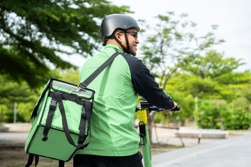 Rider food delivery man wearing green uniform and helmet ride the EV scooter delivery food service to customer. Happy delivery man with green backpack shipping of goods to customers by scooter