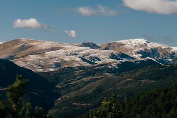 Expansive mountain range covered partially in early snow seen under a bright blue sky