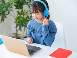 ヘッドホンをつけてノートパソコンで勉強する女の子