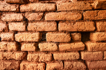 Close up of an old, weathered, red brick wall, highlighting the texture and deterioration of the...