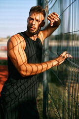 Athletic man leaning on a metal fence in a sports center