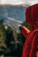 Close-up of traveler wearing winter clothes and gloves is holding a piece of thin, transparent ice with distant blurred mountain range in background