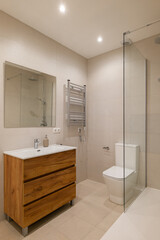 Bathroom with beige tiled walls, wood vanity with white sink, glass shower and chrome fixtures