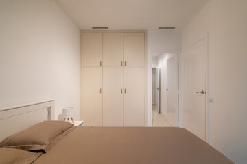 Minimalist bedroom view with taupe bedding, white built-in wardrobe and clean neutral walls