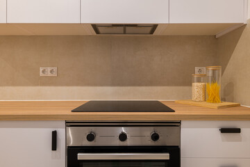Straight-on view of kitchen stove, glass cooktop, white cabinetry and wood counter with jars