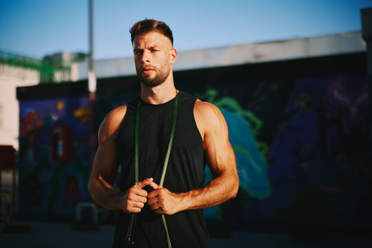 Determined male athlete holding jump rope, preparing for urban fitness training