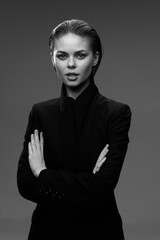 black and white portrait of serious woman in black suit with crossed arms against plain background...