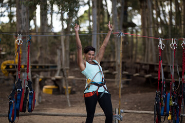 African American woman wearing safety harness and celebrating on forest ropes course
